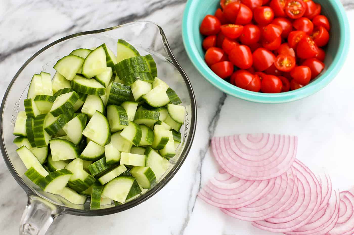 A bowl of chopped cucumber and a bowl of grape tomatoes cut in half