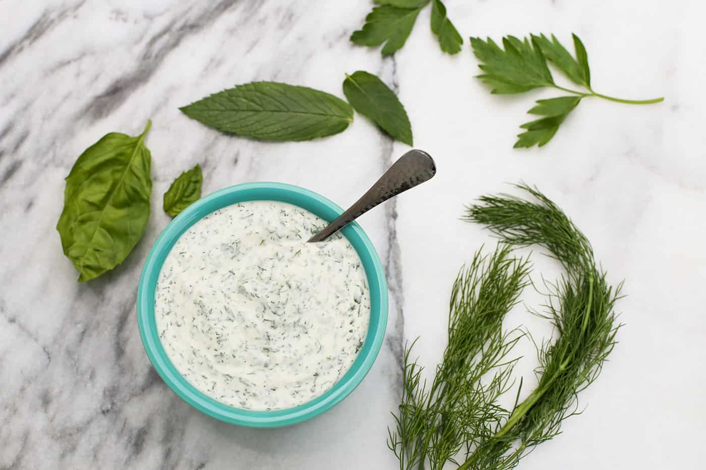 A bowl of creamy herb dressing surrounded by fresh herbs