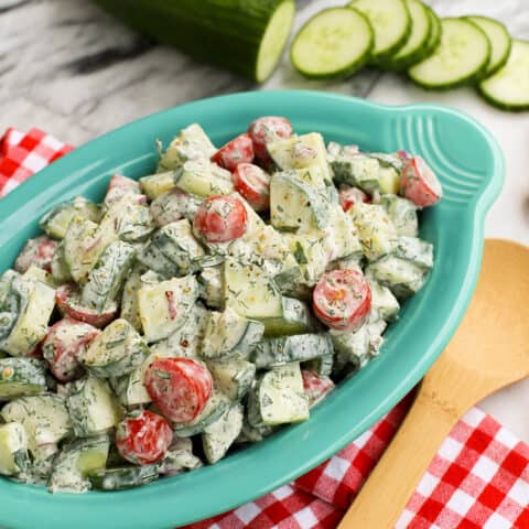 An oval serving bowl of cucumber and tomato salad