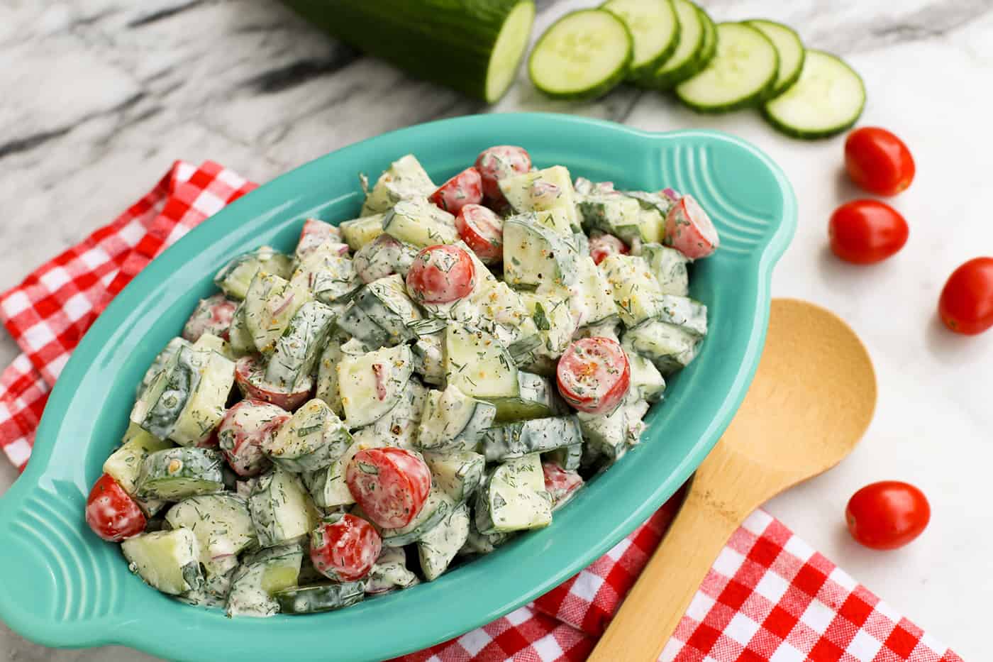 An oval serving bowl of cucumber and tomato salad