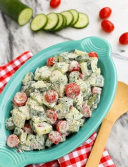 An oval serving bowl of cucumber and tomato salad