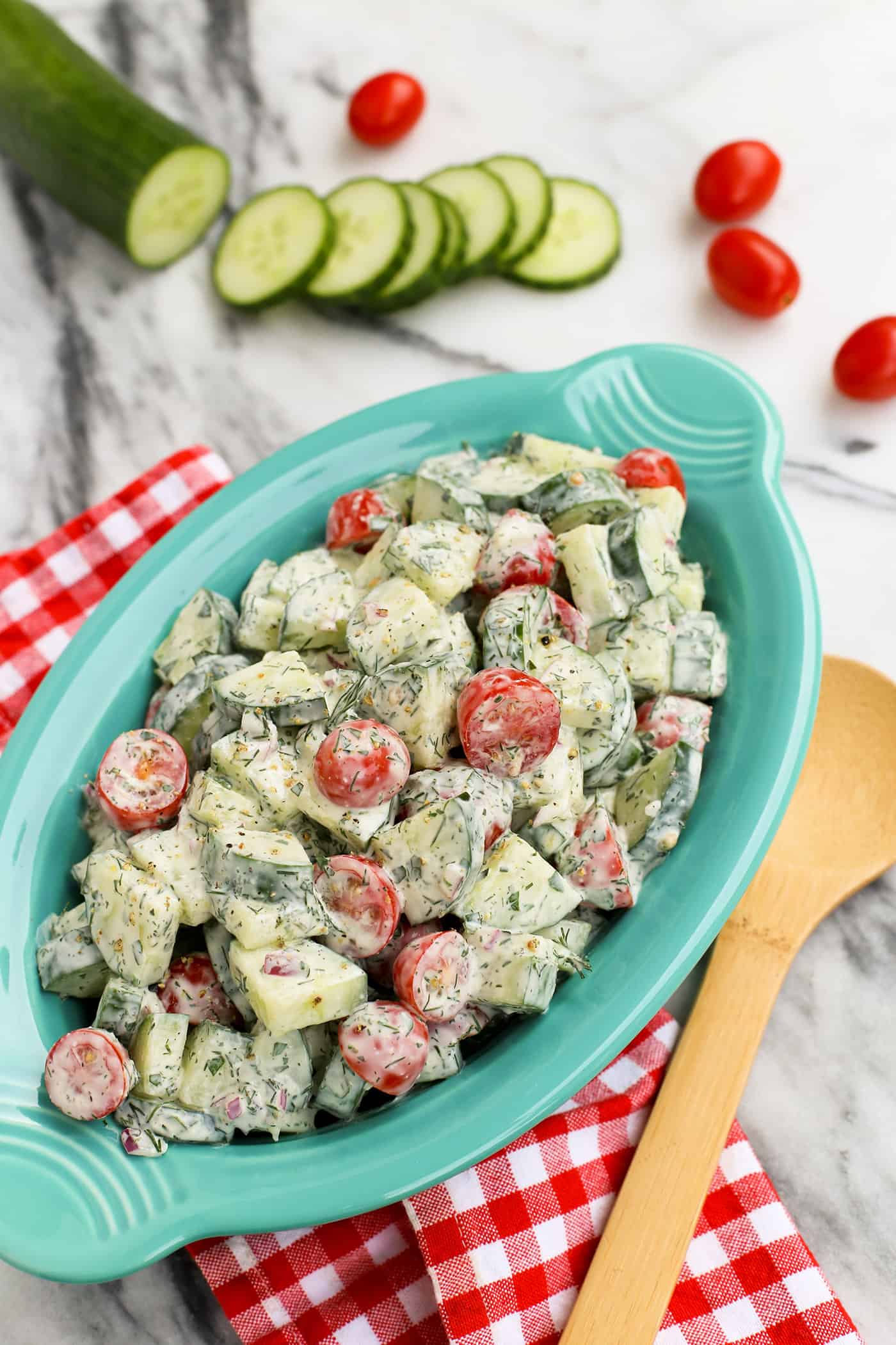 An oval serving bowl of cucumber and tomato salad