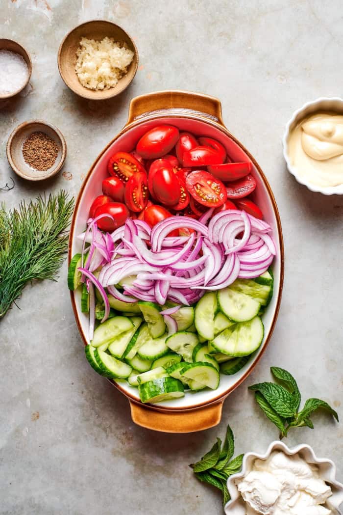 With fresh vegetables and a creamy herbed dressing, this cucumber and tomato salad is the perfect goes-with-anything side dish for summer. Tomatoes, red onion, and cucumber in bowl.
