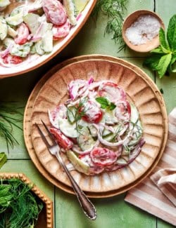 Creamy cucumber and tomato salad with fresh herbs on plate.