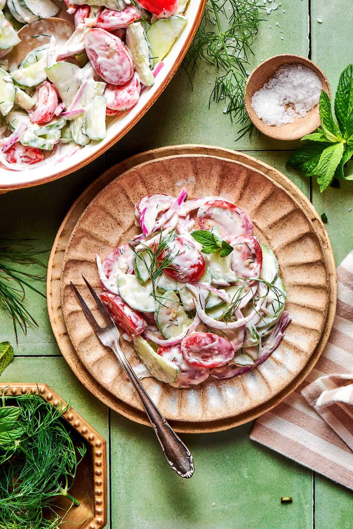 With fresh vegetables and a creamy herbed dressing, this cucumber and tomato salad is the perfect goes-with-anything side dish for summer. Creamy cucumber and tomato salad with fresh herbs on plate.
