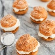 Pumpkin Pie Cream Puffs on a marble table sprinkled with powered sugar