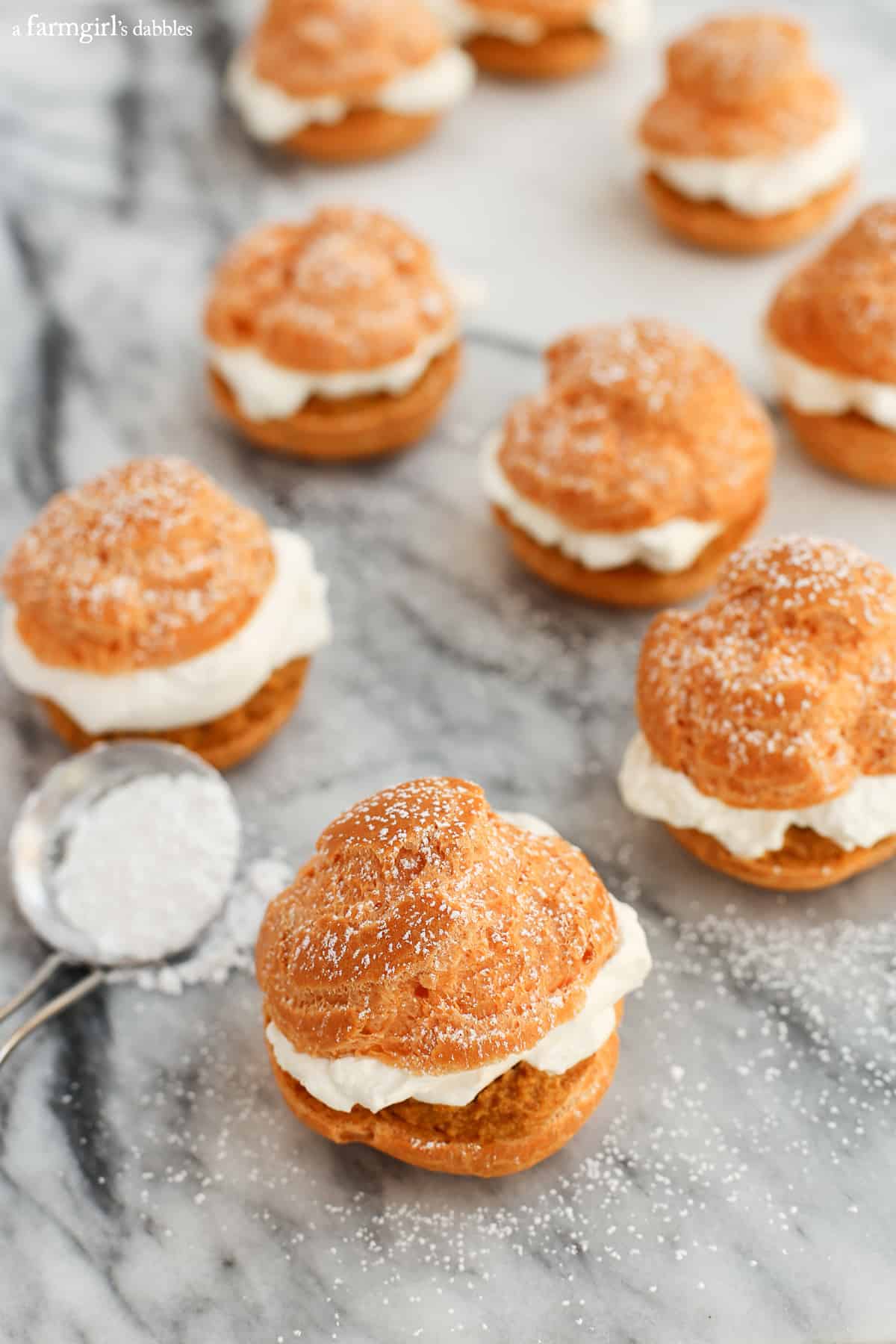 Pumpkin Pie Cream Puffs on a marble table sprinkled with powered sugar.
