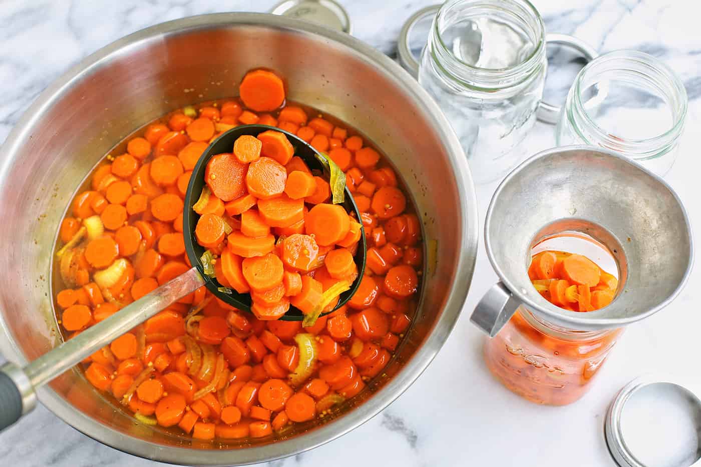 A ladle scooping cooked carrots into a mason jar