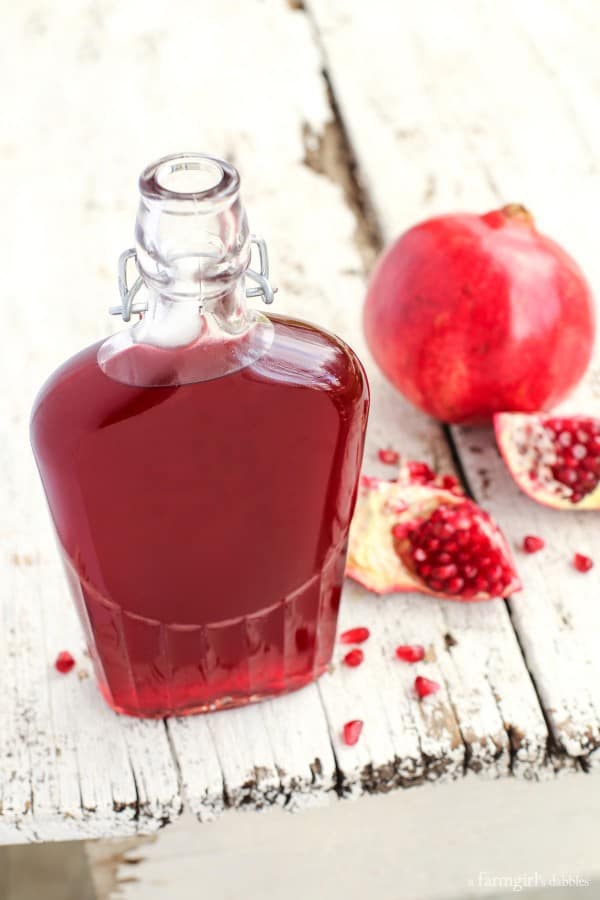 a glass bottle of pomegranate shrub with pomegranate seeds