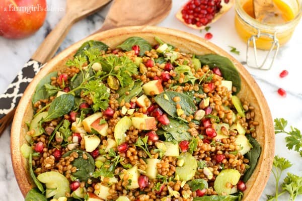 Wheat Berry and Spinach Salad with a jar of Orange-Curry Vinaigrette and fresh pomegranate and apples