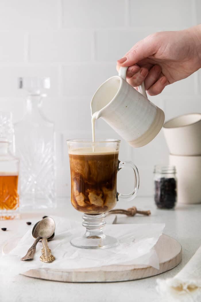 Cream being poured into a hot buttered rum coffee cocktai;