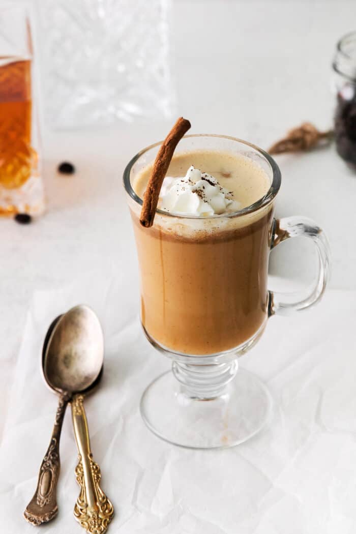 A hot buttered rum coffee cocktail with whipped cream and a cinnamon stick