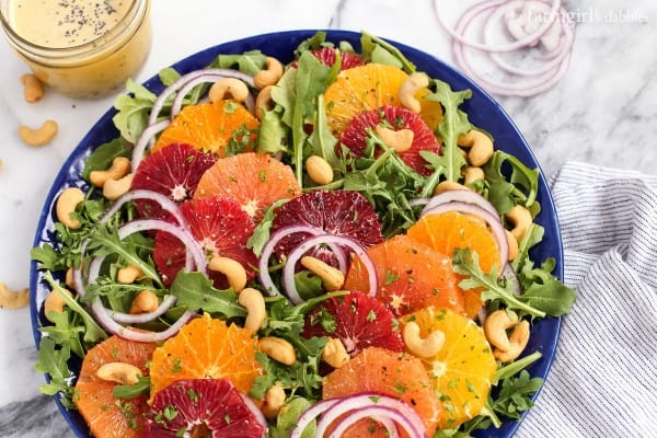 a blue bowl of Citrus Salad with a mason jar of Orange Poppy Seed Dressing