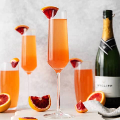 Blood orange mimosas next to a bottle of champagne