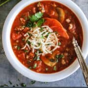 pinterest image of a bowl of cheesy pizza soup with homemade garlic cheesy bread