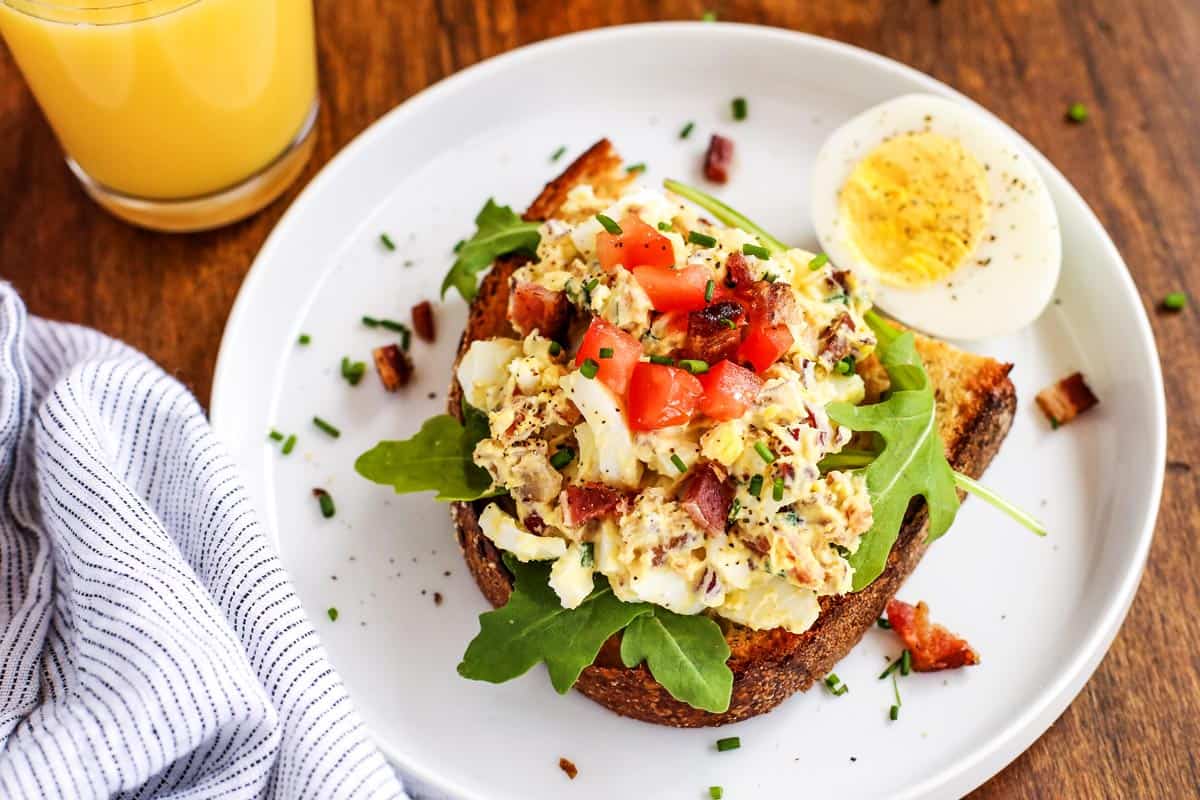 egg salad on toast on a white plate and a glass of orange juice