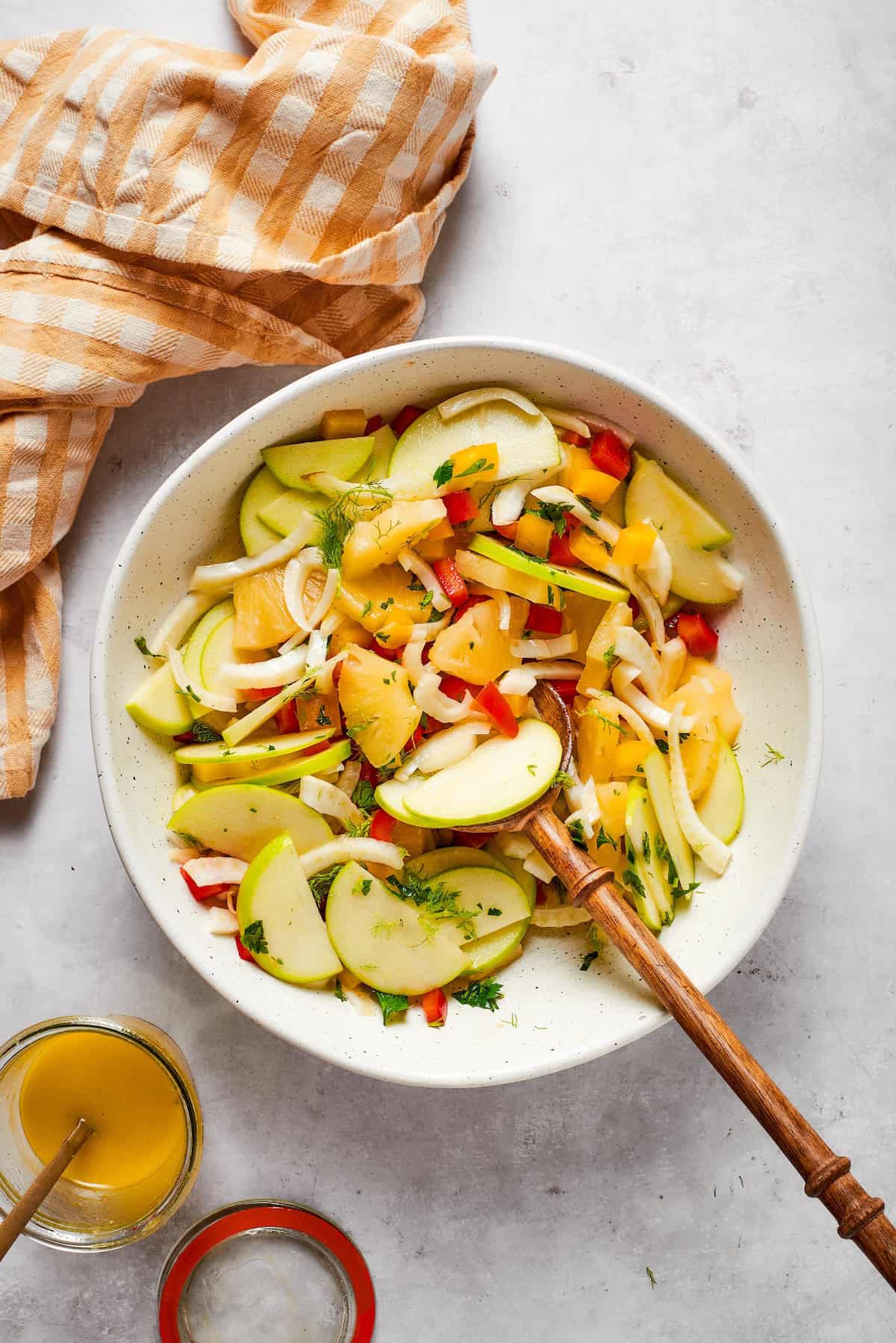 Spoon in bowl of fennel apple salad with jar of dressing on the side.