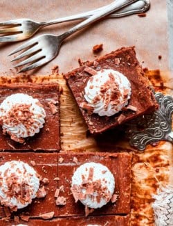 Sliced Nutella cheesecake bars topped with whipped cream and chocolate shavings.