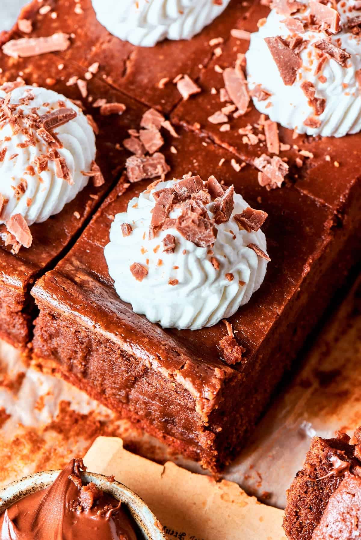 Sliced Nutella cheesecake bars topped with whipped cream and chocolate shavings.