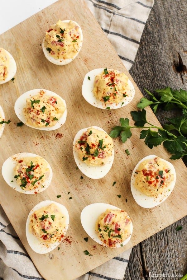 Smoky Tomato Deviled Eggs on a wood board with fresh cilantro