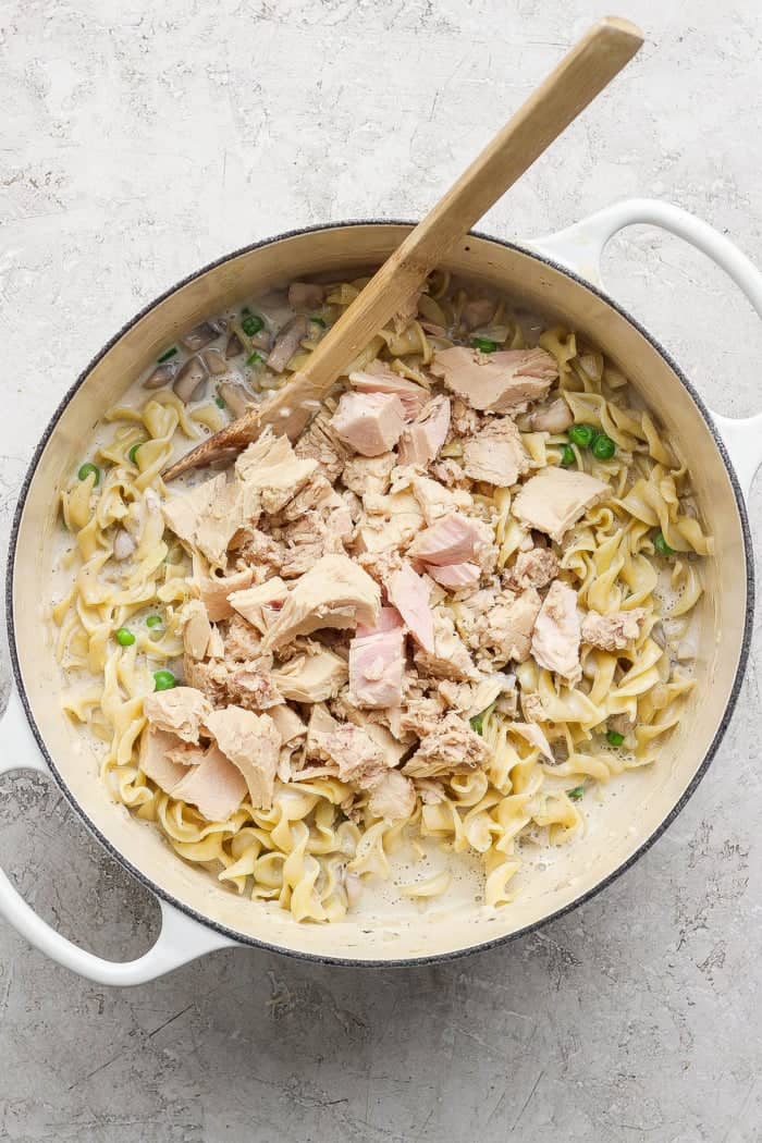 This sour cream and onion tuna noodle casserole is creamy, comforting and delicious. It’s an easy, nostalgic dinner with a bold flavor twist! Tuna chunks added to sour cream and onion tuna noodle casserole mixture in Dutch oven.