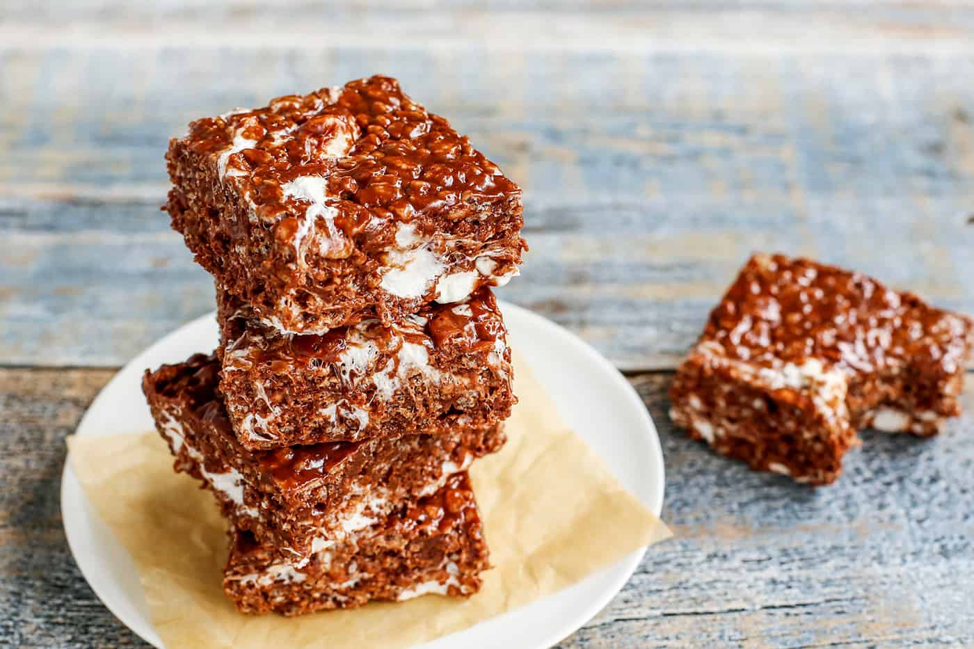 3 chocolate peanut butter rice krispies bars on a plate with another bar on the table, with a bite taken from it