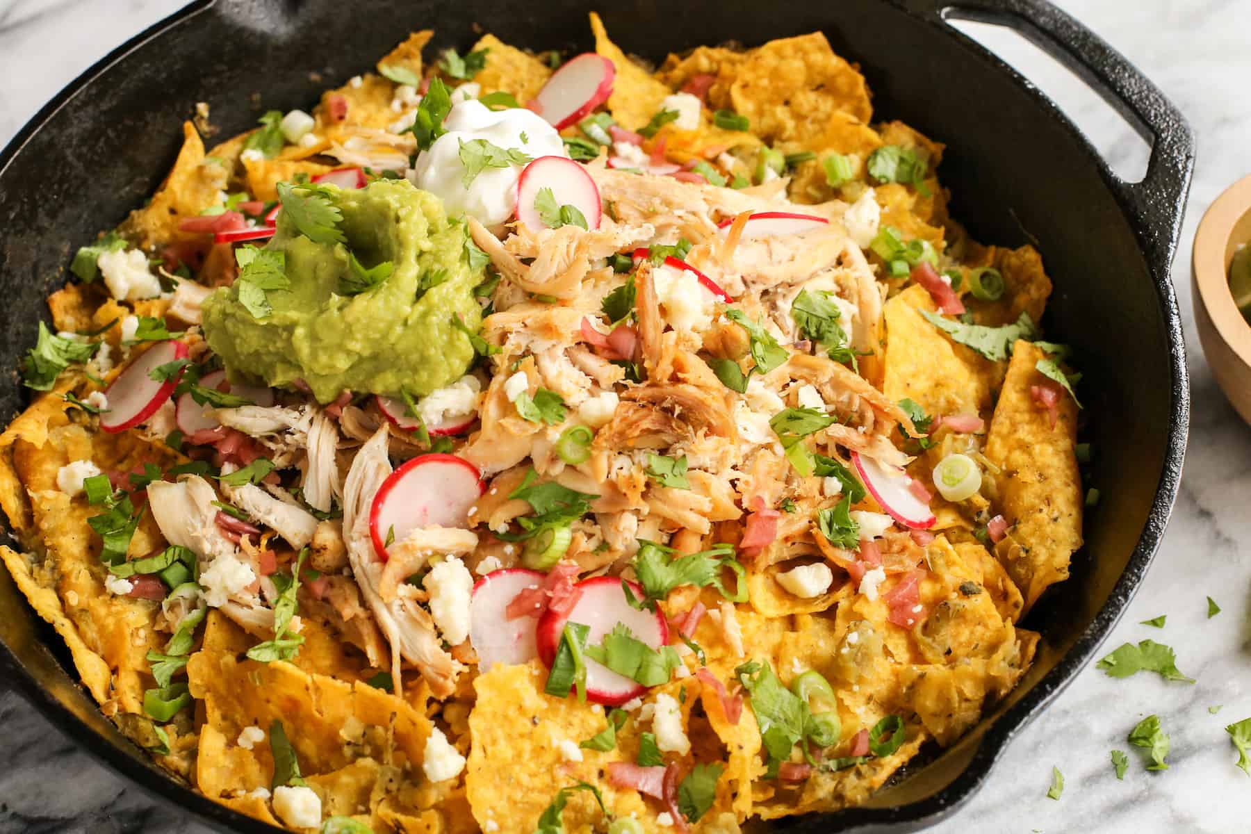 Skillet chilaquiles verdes topped with chicken and sliced radishes