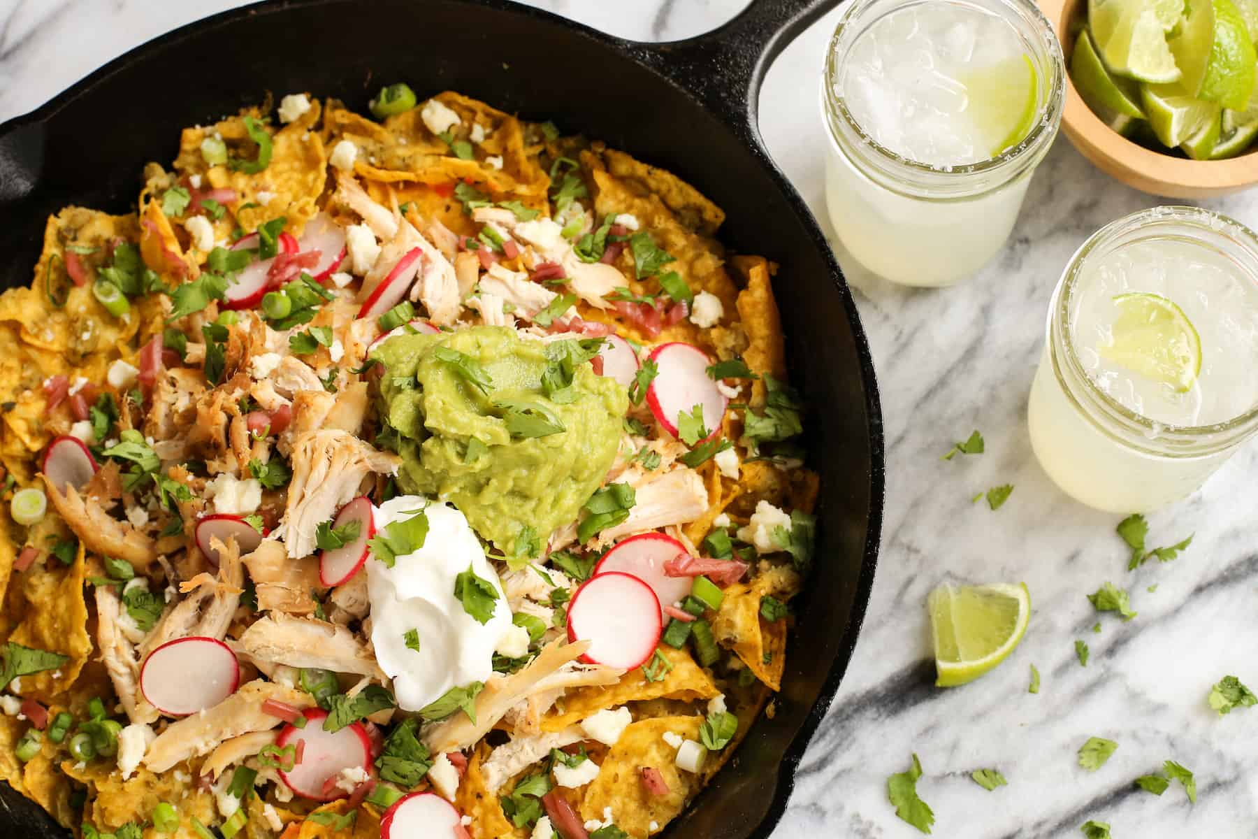 Overhead view of skillet chicken chilaquiles topped with guacamole and sliced radishes