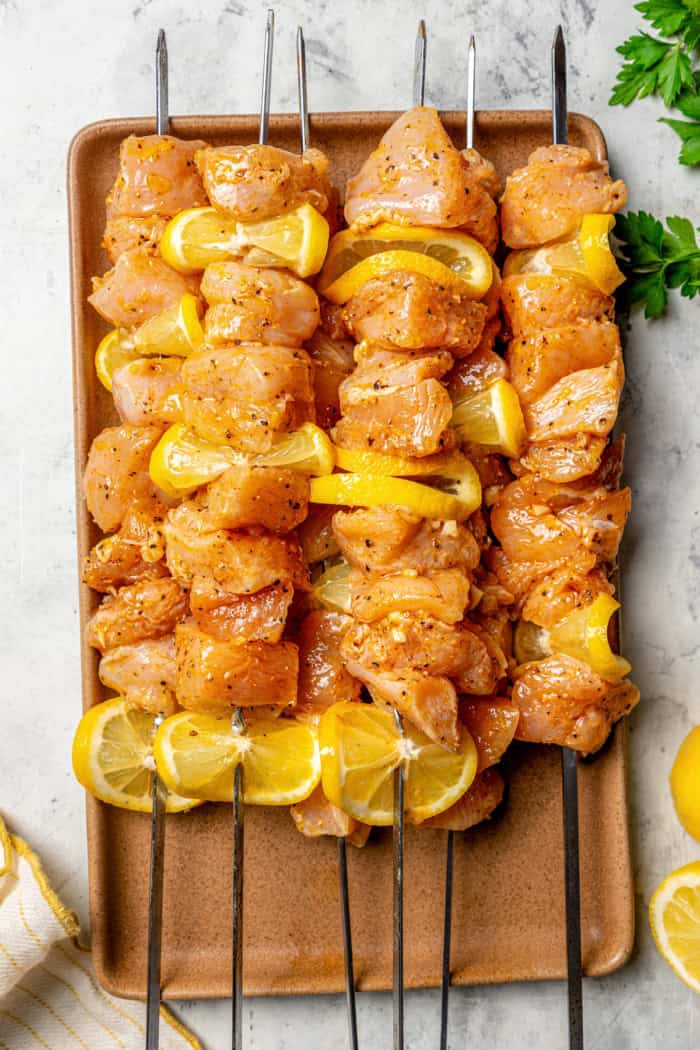 These Grilled Lemon Pepper Chicken Skewers are an easy summer recipe that's super fast for a weeknight. Don't skip the lemon butter sauce! Lemon pepper chicken skewers on wooden board before cooking