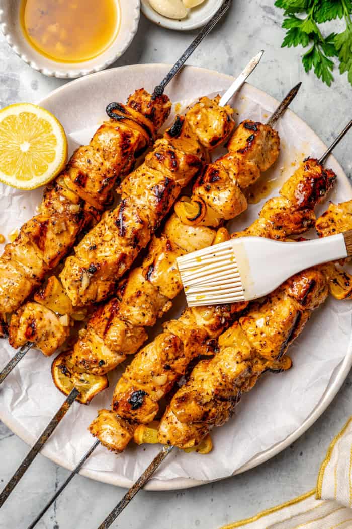 Brushing lemon butter sauce onto lemon pepper chicken skewers