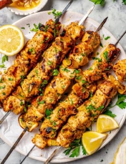 Grilled lemon pepper chicken skewers on platter with lemon wedges