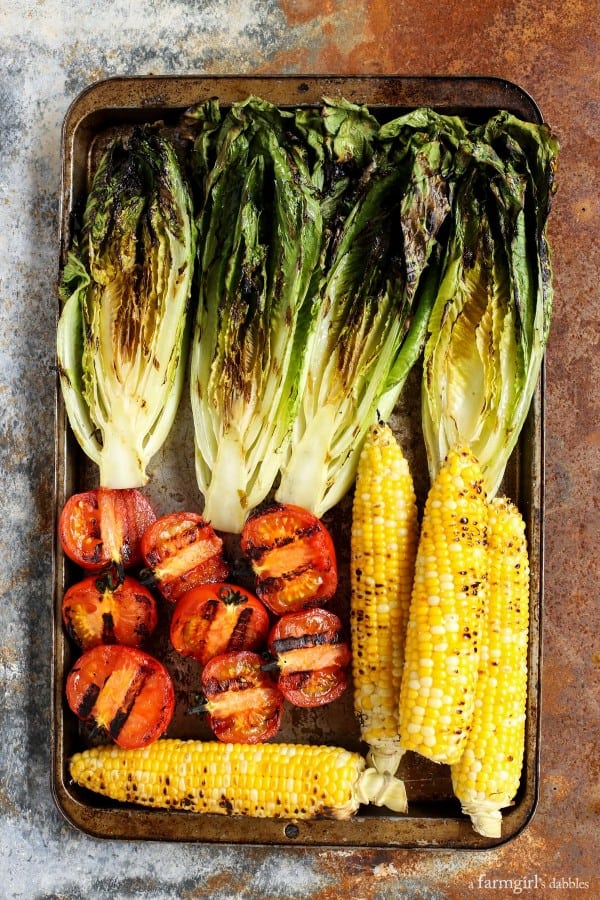 grilled romaine, corn on the cob, and tomatoes on a pan