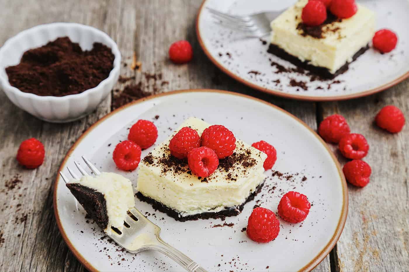 A black and white cheesecake square on a white plate with one bite on a fork.