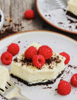 A black and white cheesecake bar topped with fresh raspberries on a white plate.