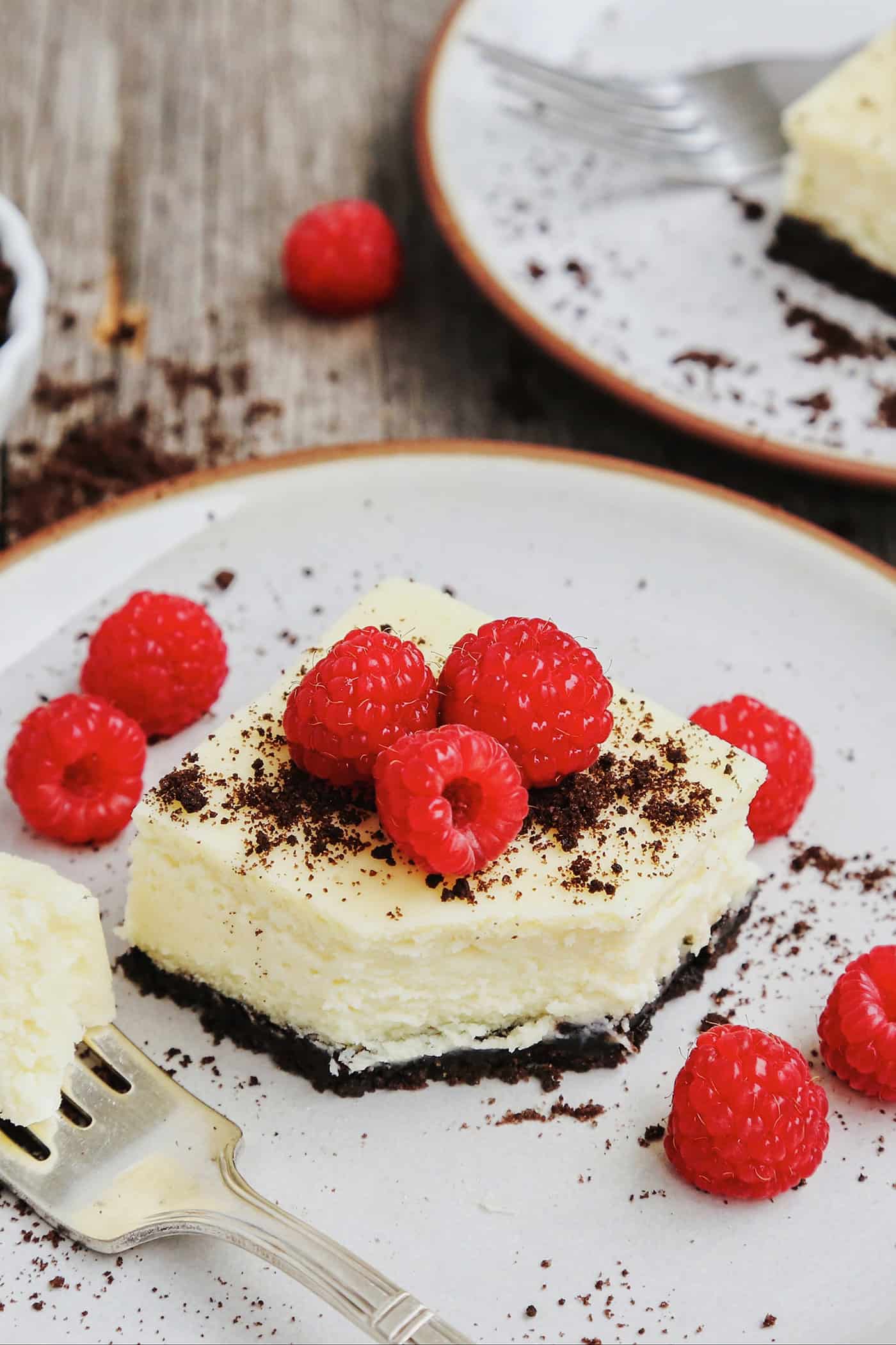 A black and white cheesecake bar topped with fresh raspberries on a white plate.