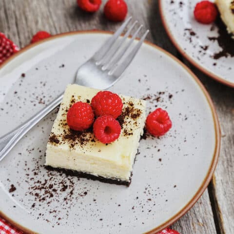 An oreo cheesecake square on a white plate topped with fresh raspberries