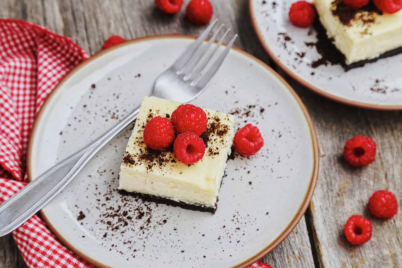 An oreo cheesecake square on a white plate topped with fresh raspberries