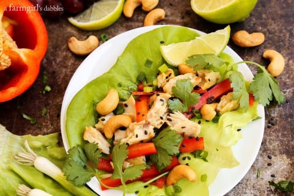 Large lettuce leaf on a plate filled with shredded tilapia, red peppers, cashews and cilantro