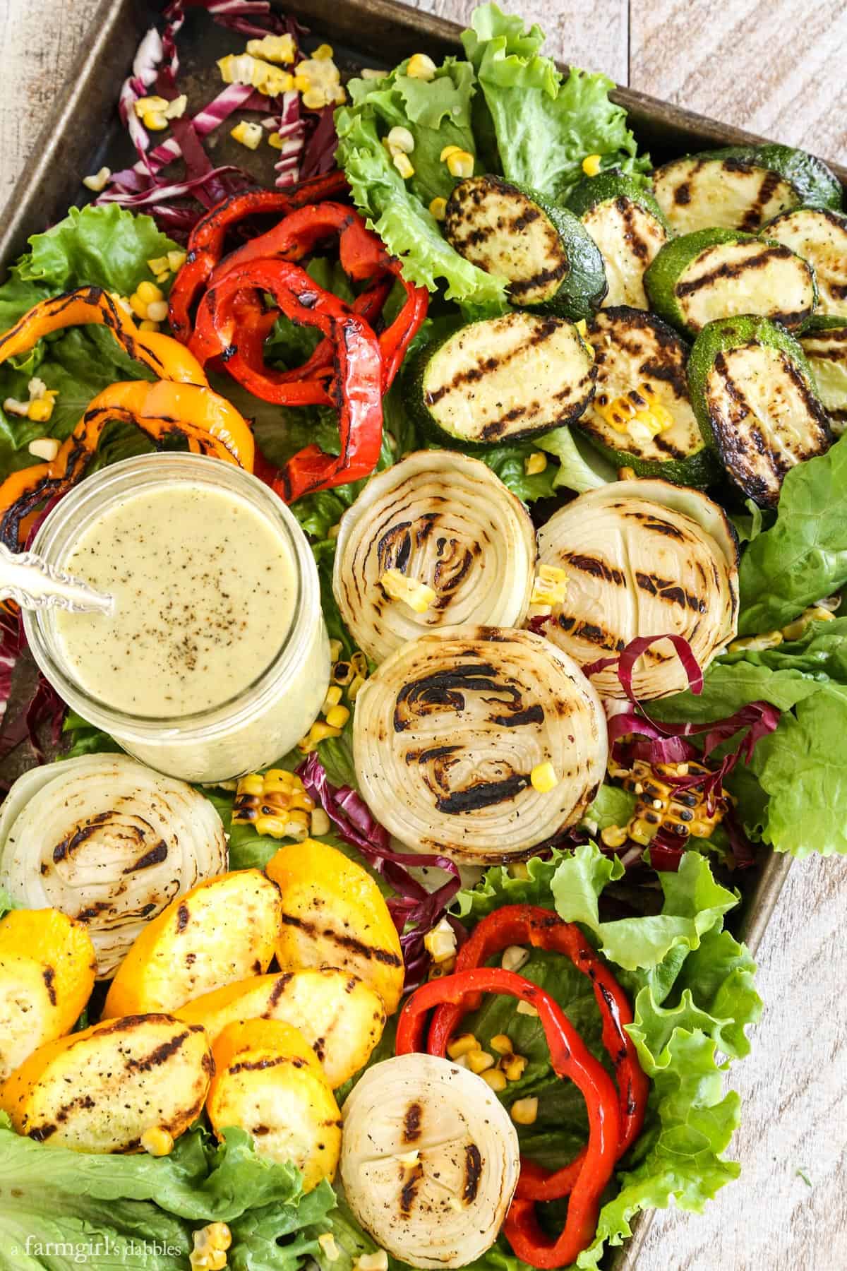This grilled veggie salad with grilled vidalia onion dressing includes fresh zucchini, colorful bell peppers, sweet corn, and more! Grilled Veggies Salad with Grilled Vidalia Onion Dressing on a rimmed baking sheet.