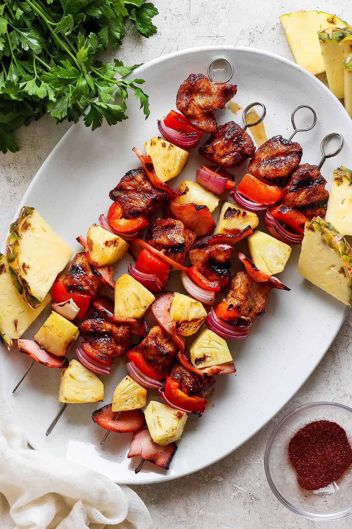 Grilled Hawaiian chicken kabobs have the perfect balance of heat and sweet, with pineapple, red pepper, red onions and savory bacon. Yum! Overhead view of Hawaiian chicken chili kabobs on platter