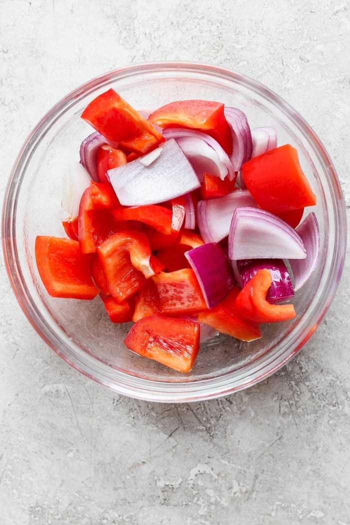 Overhead view of red bell pepper and red onion pieces in glass bowl