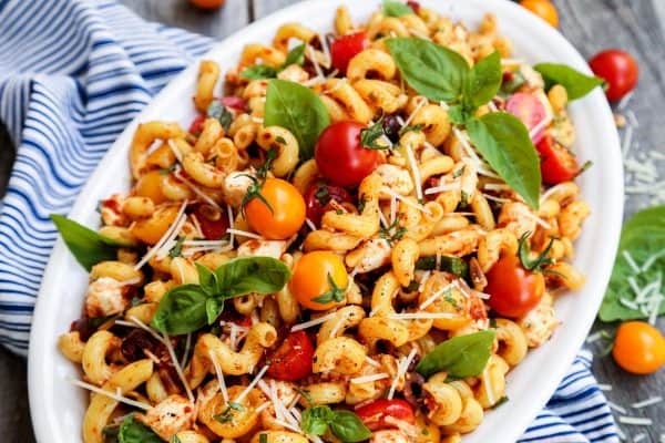 a serving bowl of full of pasta in a sun dried tomato dressing, with fresh tomatoes and basil