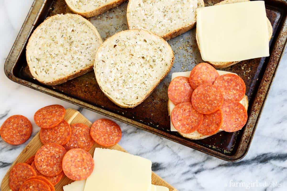 Landscape photo of adding the mozzarella and pepperoni over the bread on a baking sheet. 
