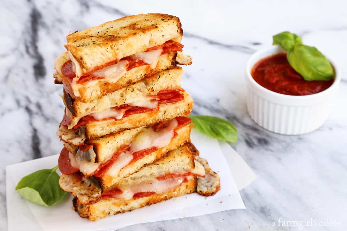 Landscape photo of grilled cheese halves with salty pepperoni and sweet tomato sauce for dipping on the side. 