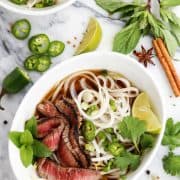 Quick Grilled Beef Pho in a white bowl with fresh cilantro, mint, and lime