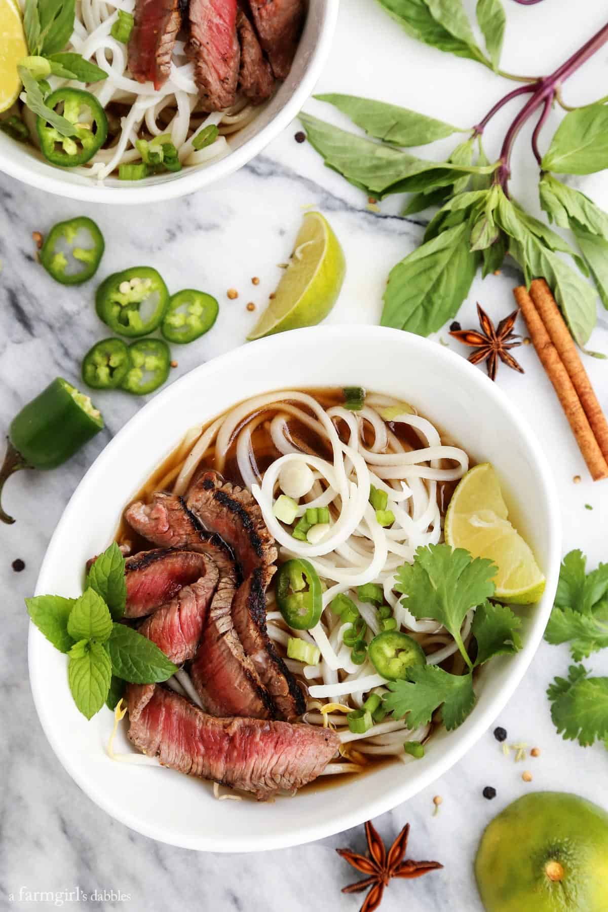 Quick Grilled Beef Pho in a white bowl with fresh cilantro, mint, and lime