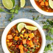 Overhead view of bowls of beef stew with sweet potatoes garnished with lime wedges.