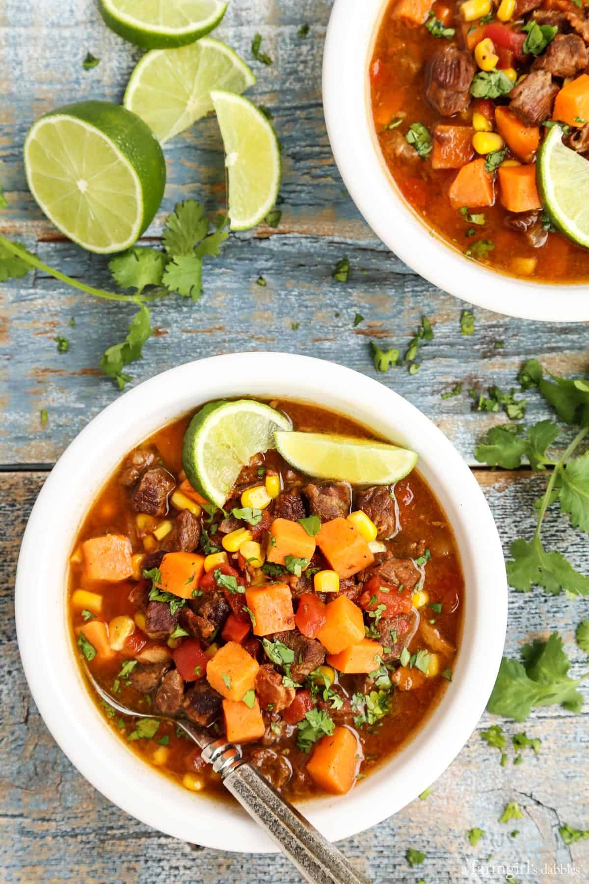 Overhead view of bowls of beef stew with sweet potatoes garnished with lime wedges.