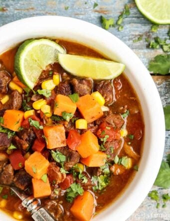Overhead view of a bowl of beef stew with sweet potatoes garnished with lime wedges.