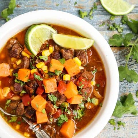 Overhead view of a bowl of beef stew with sweet potatoes garnished with lime wedges.